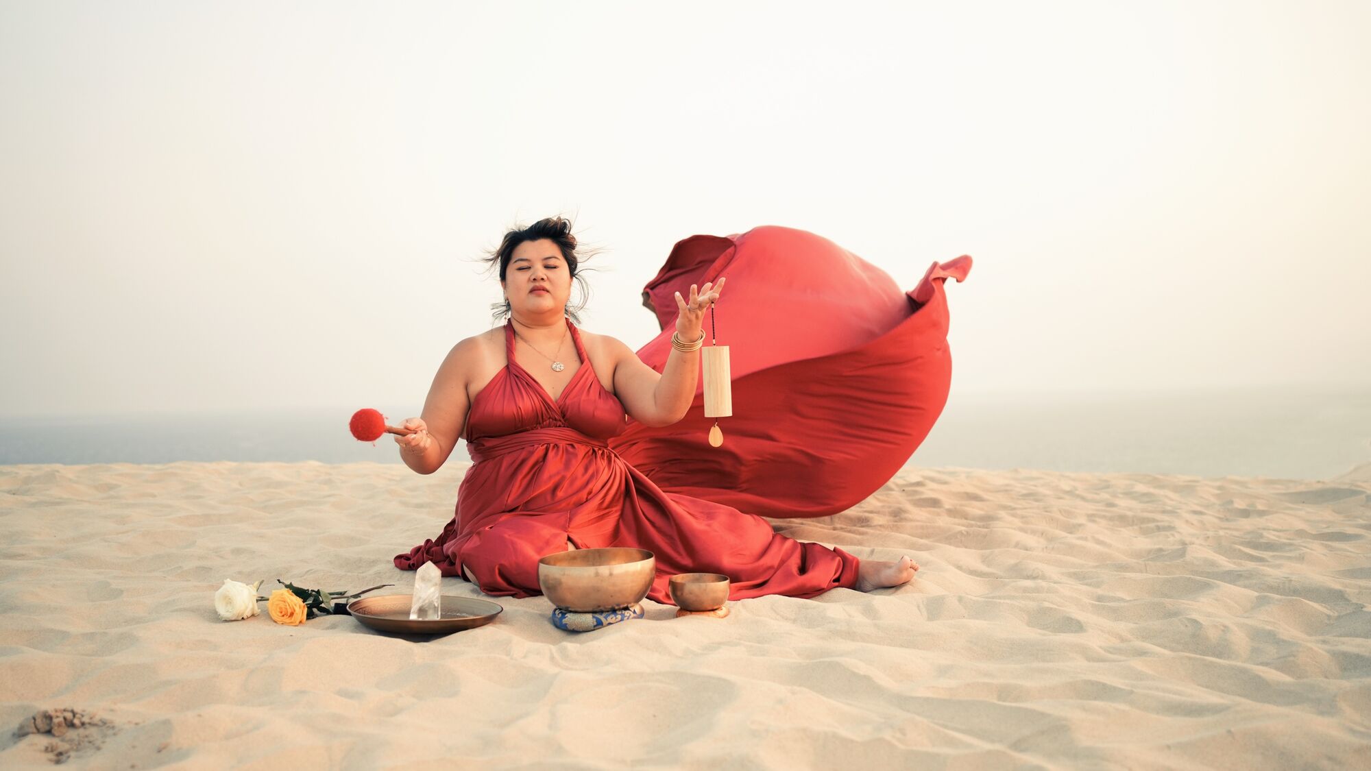 Vivi playing singing bowls and a wind chime on a sand dune in Qatar